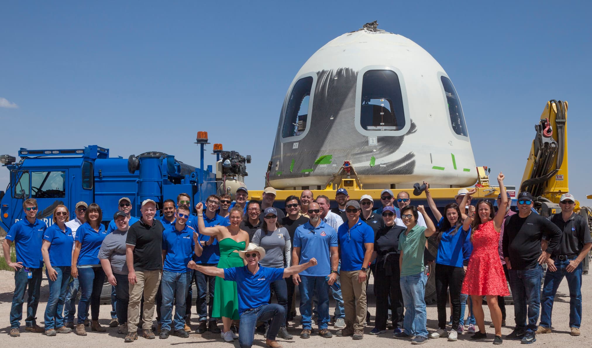 Blue Origin employees celebrate in front of a New Shepard crew capsule loaded onto a transporter following a successful flight.