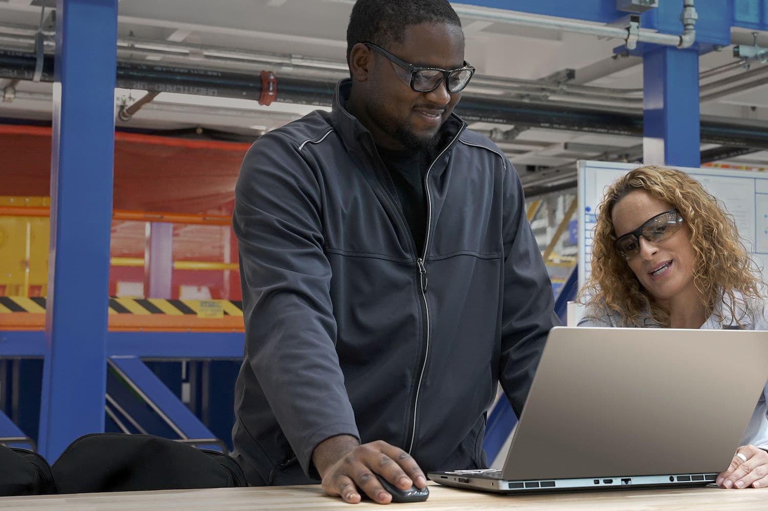 Two employees wearing safety glasses look at a laptop screen.